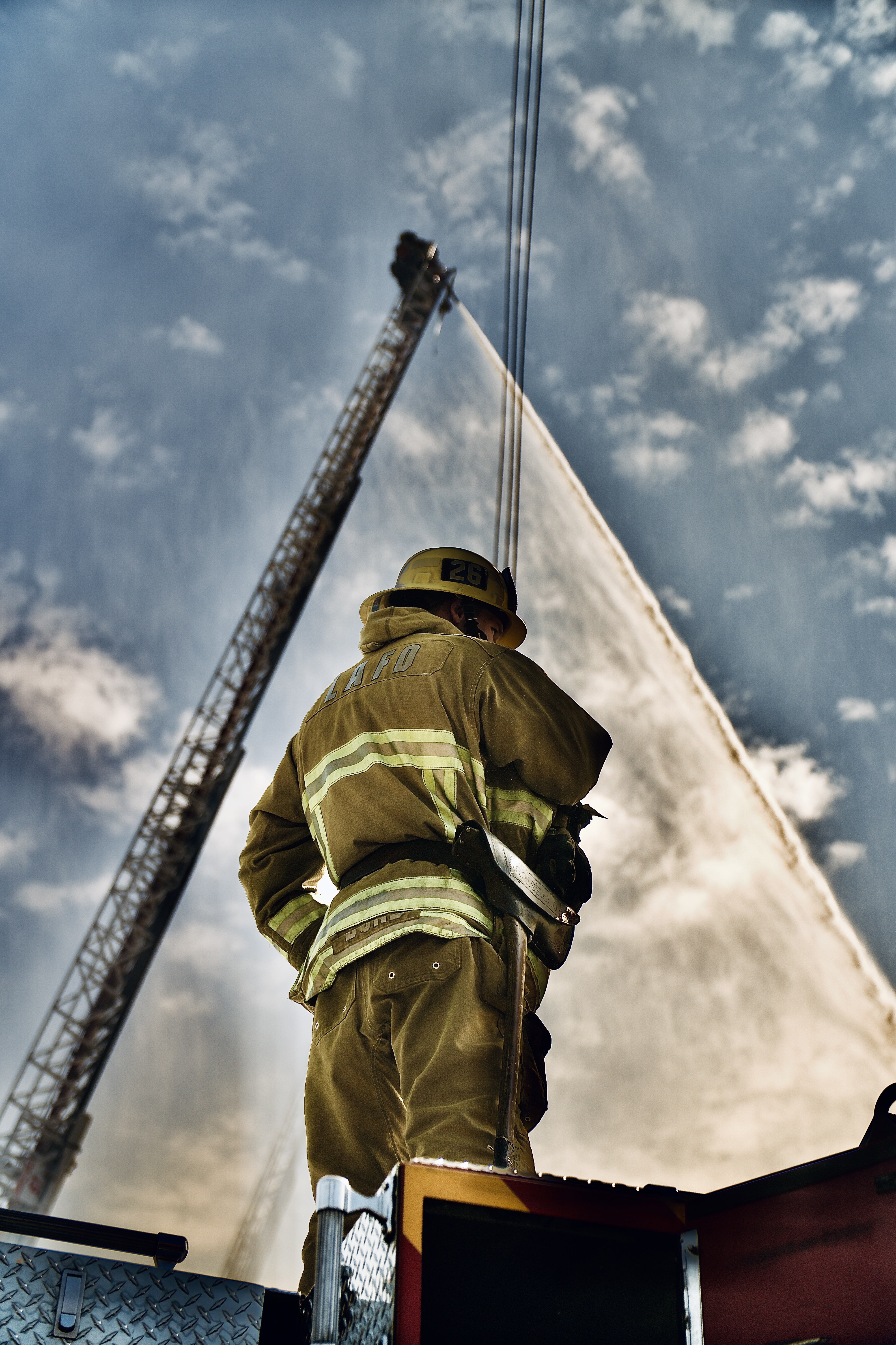 Firefighter standing on fire truck with aerial ladder in the background