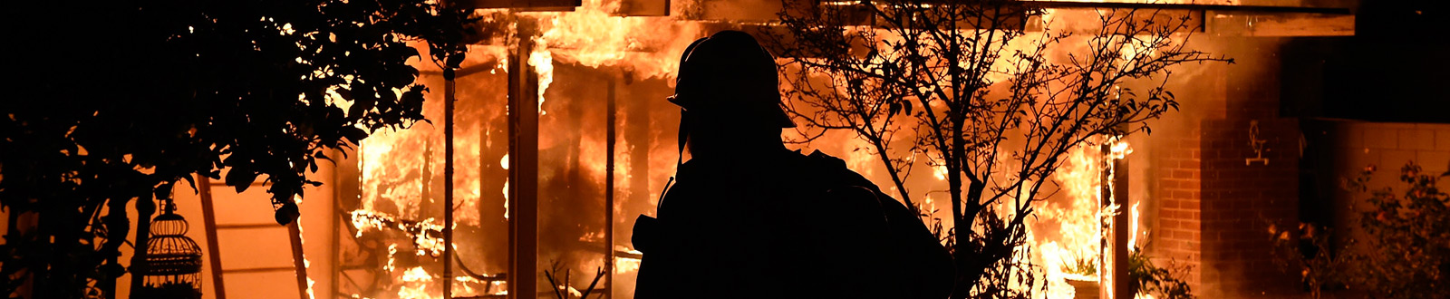 A firefighter silhouetted by a burning house 